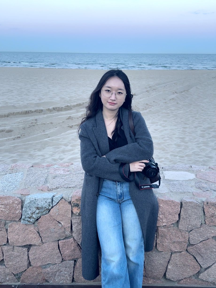 Liu Yanxin standing by the sea with her Canon camera